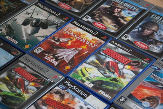 A collection of PlayStation 2 video game cases arranged closely together, featuring titles such as Ace Combat and Burnout. The cases display a mix of action and racing game covers, with vibrant images of fighter jets and cars.