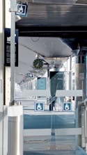 A modern train station platform with a clock showing the time. Signs indicating accessibility are visible, and the platform appears empty.