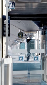 A modern train station platform with a clock showing the time. Signs indicating accessibility are visible, and the platform appears empty.