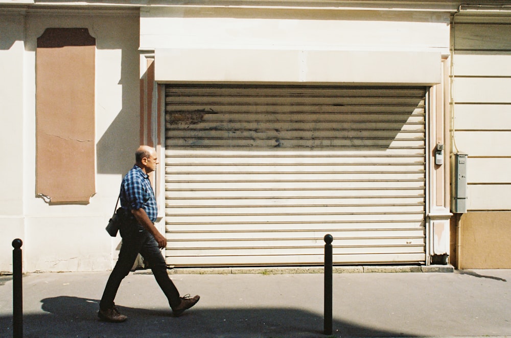 man in blue and white plaid dress shirt and black pants standing near white roll up