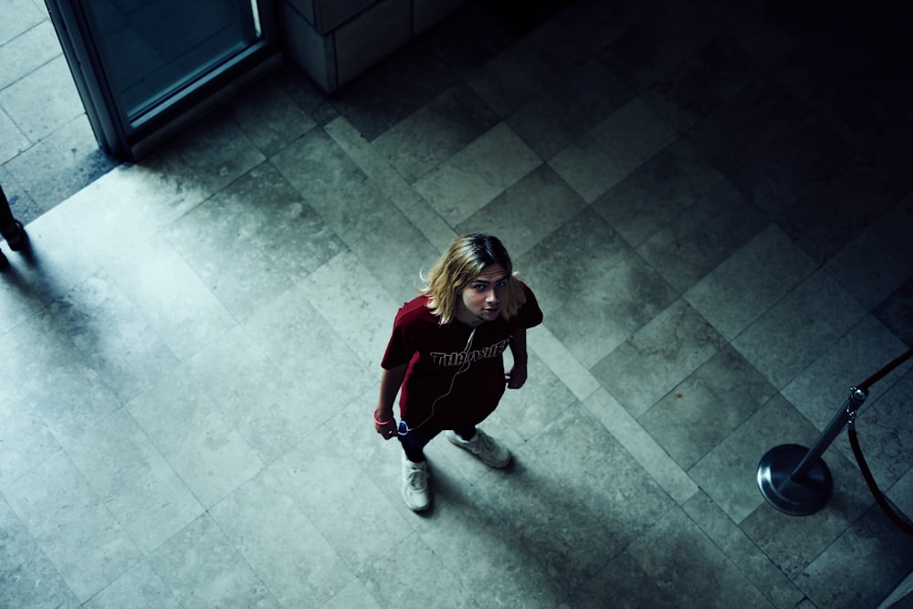 girl in red long sleeve shirt and black pants sitting on gray concrete floor