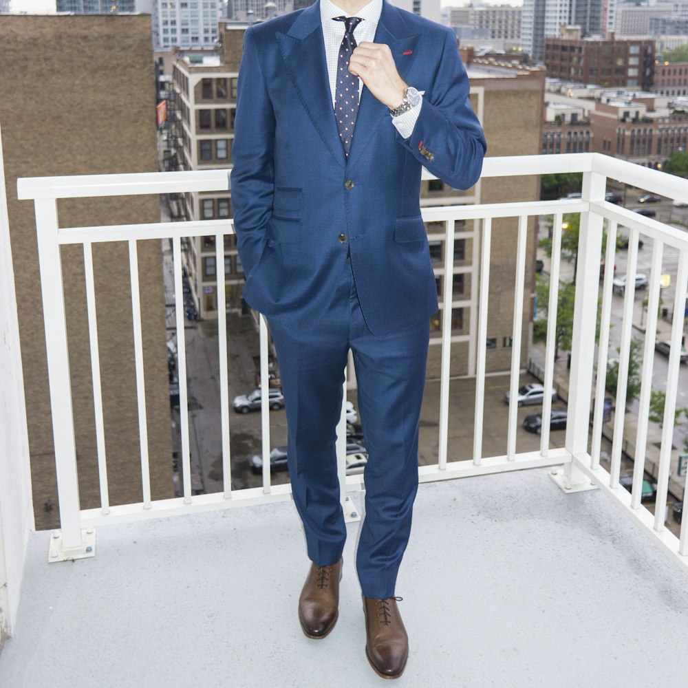 man in blue suit standing near white wooden fence during daytime