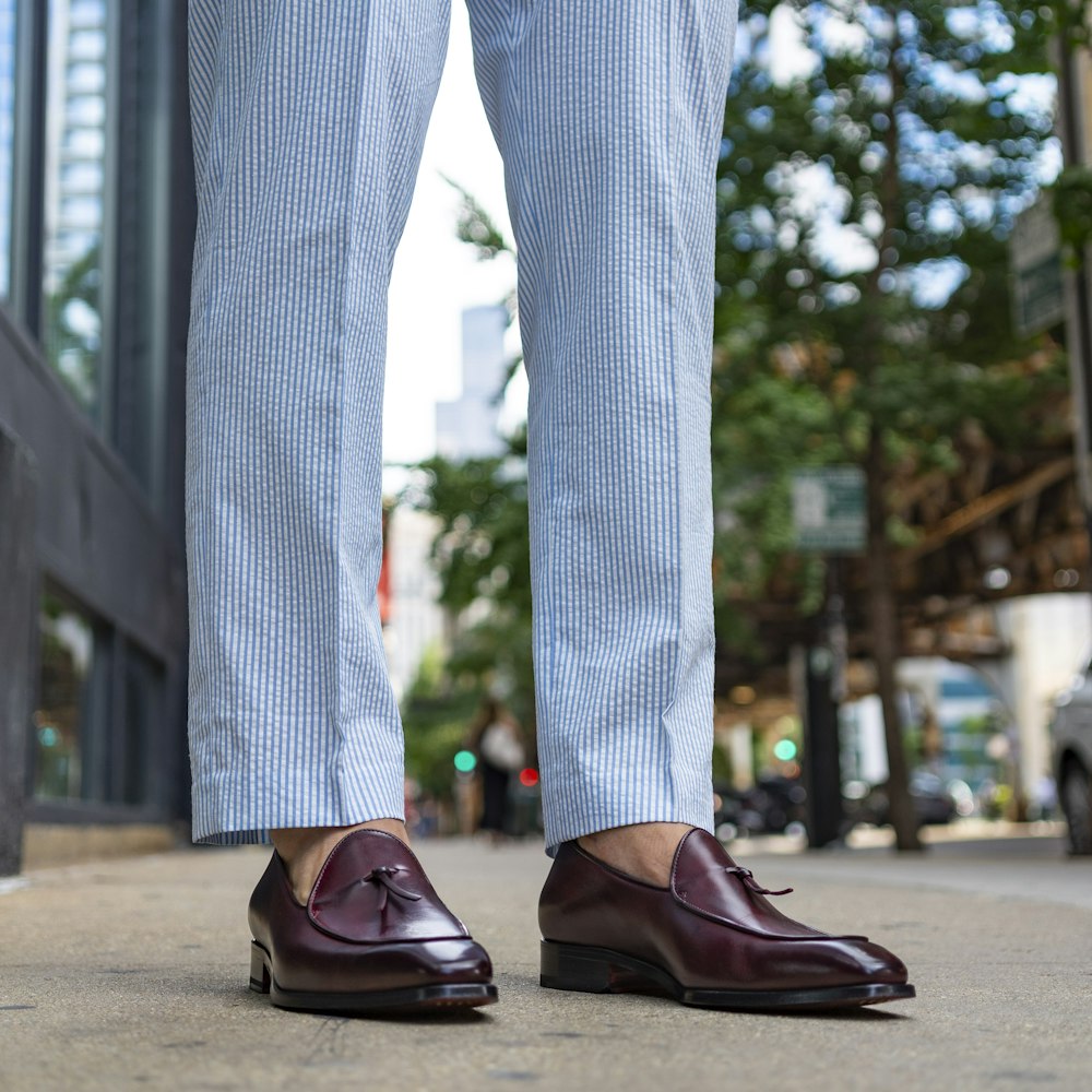 woman in blue and white floral pants and brown leather shoes standing on gray concrete floor