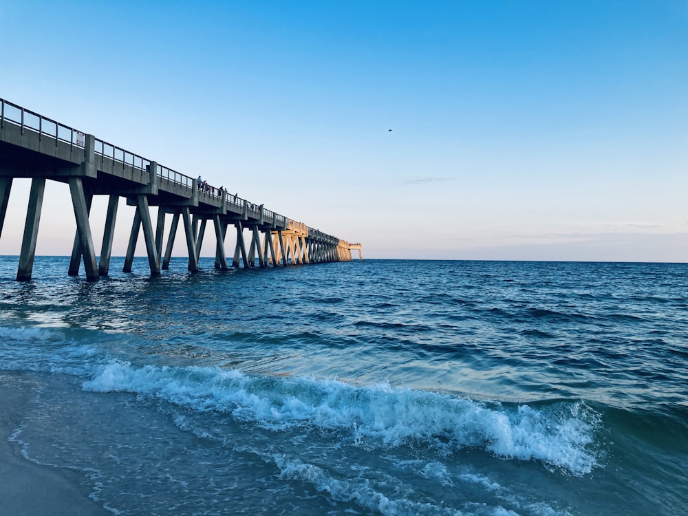 sea waves crashing on beach dock under blue sky during daytime