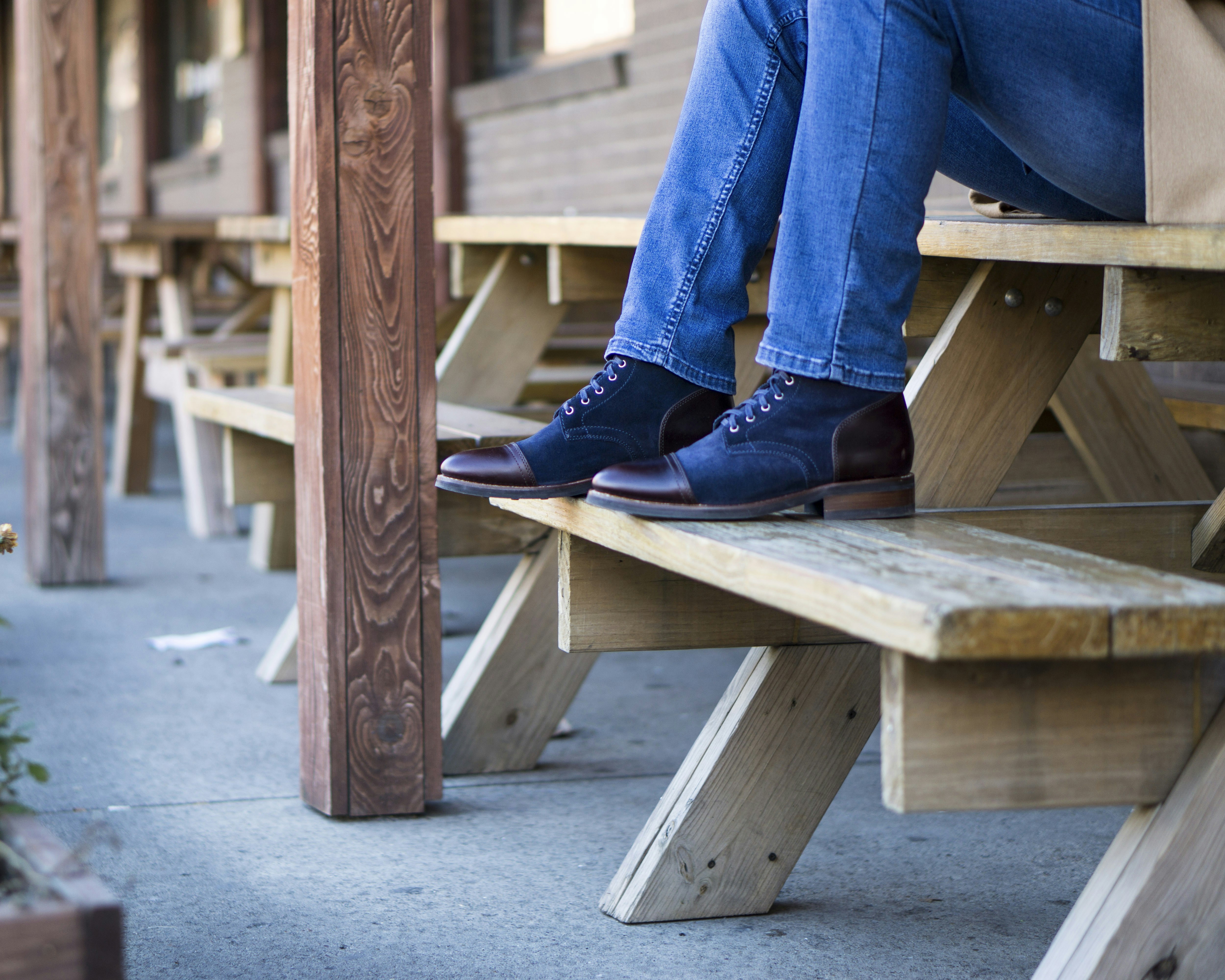 person in blue denim jeans and black leather boots sitting on brown wooden bench