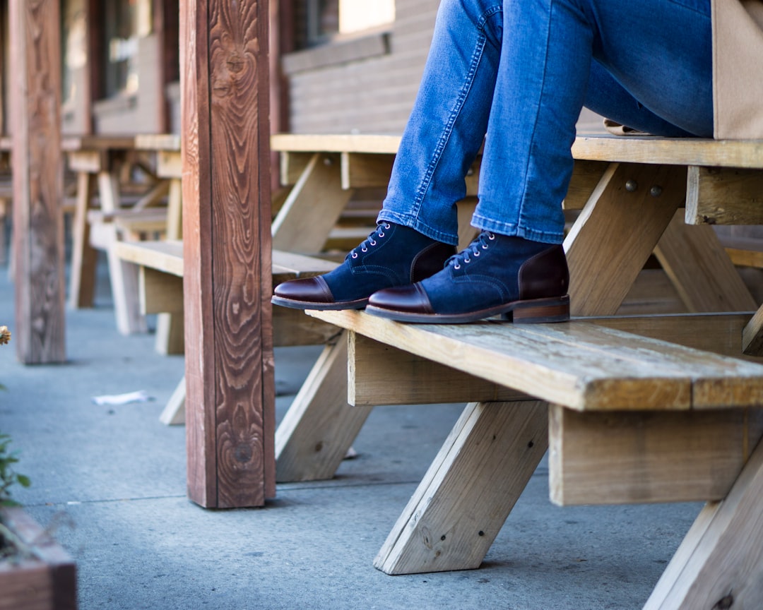 person in blue denim jeans and black leather boots sitting on brown wooden bench