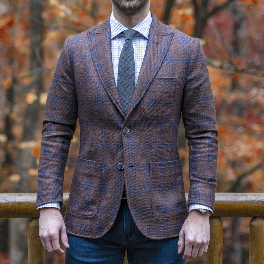 man in brown and gray pinstripe suit jacket and blue denim jeans standing beside brown wooden