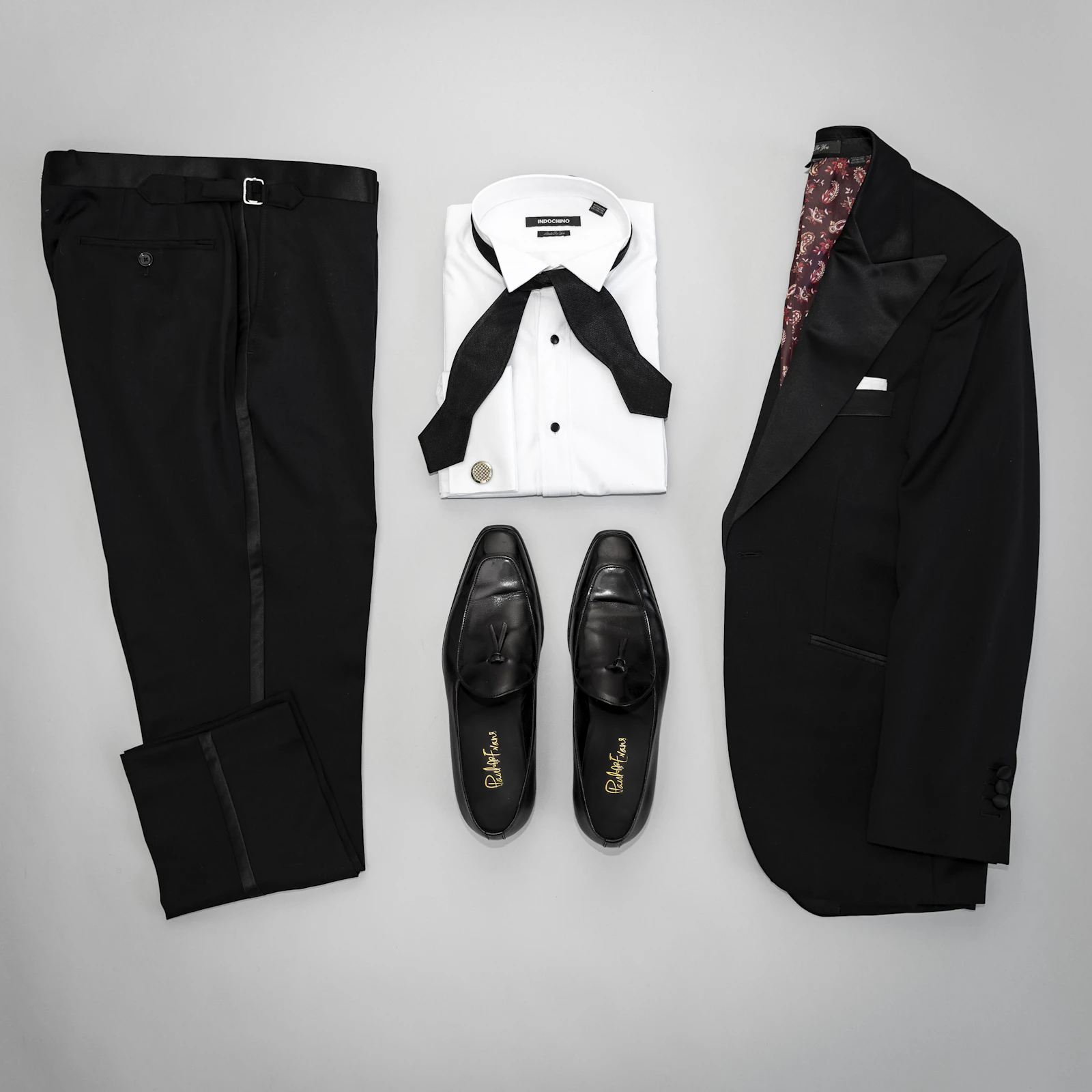 Black-tie flatlay with a tuxedo, bow tie, cufflinks and tassel loafers on a white surface, a real stock photo with no people in it, used as a stand-in for the James Bond casting story. It is not a still from any film and not a photo of any actor