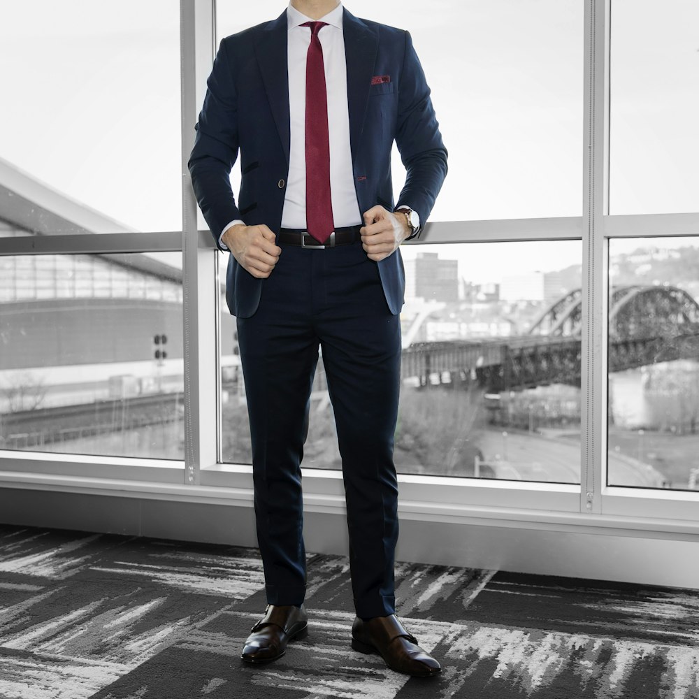 man in blue dress shirt and blue denim jeans standing near glass window