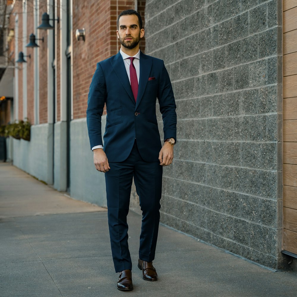 man in black suit standing beside gray concrete wall during daytime