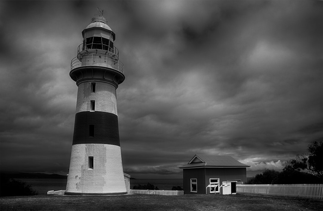 grayscale photo of lighthouse under cloudy sky