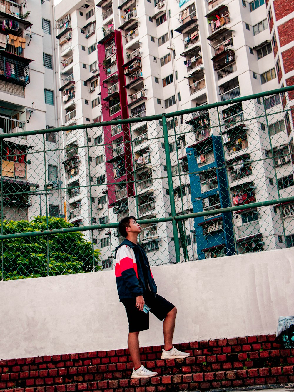 man in blue and red crew neck t-shirt and black shorts standing on gray concrete