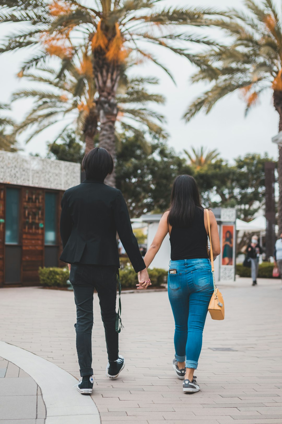 man in black suit jacket and woman in blue denim jeans walking on sidewalk during daytime