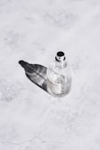 Glossy rose gold perfume bottle resting on a light gray marble surface with gentle shadows.
