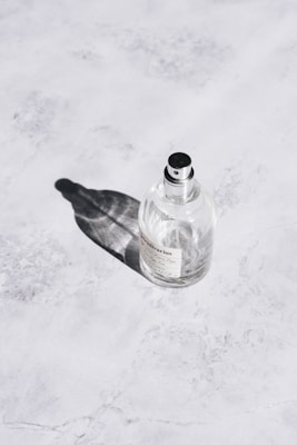 Close-up of a sleek black and gold perfume bottle resting on a white marble surface with soft natural light.