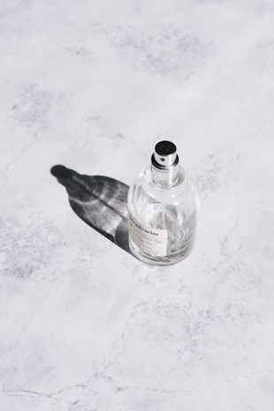 Close-up of a sleek perfume bottle resting on a smooth off-white surface with mineral blue shadows.