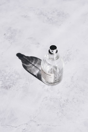 Close-up of a sleek black and gold perfume bottle resting on a white marble surface with soft natural light.