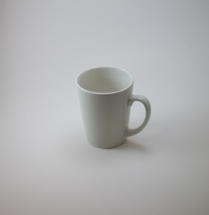 Close-up of a matte white ceramic mug with a smooth rounded handle on a wooden table