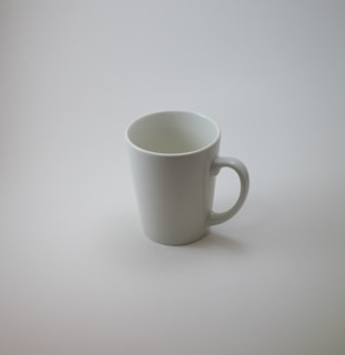 A clean, crisp white ceramic mug with a smooth curved handle on a wooden table.