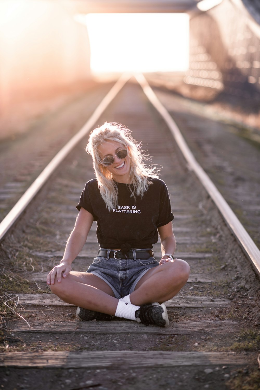 woman in black crew neck t-shirt and blue denim shorts sitting on train rail during