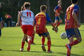 men in red and blue soccer jersey shirt running on green grass field during daytime