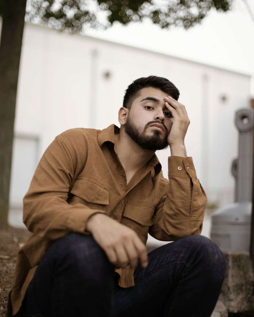 man in brown button up shirt and blue denim jeans sitting on brown concrete bench during