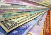 A collection of various international currencies displayed in a fanned out arrangement. The notes are colorful and include currencies from different countries, featuring intricate designs, text, and patterns.