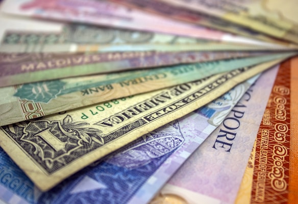 A collection of various international currencies displayed in a fanned out arrangement. The notes are colorful and include currencies from different countries, featuring intricate designs, text, and patterns.