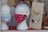 A shop window display featuring two mannequin heads wearing patterned face masks, one with floral design and the other with a pink mask decorated with cat faces. Next to them are cardboard displays holding necklaces with large, colorful beads. In the background, various small items and fabrics are visible.