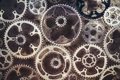 A series of overlapping metallic gears, intricately arranged, with varying sizes and shapes. The aged texture of the metal suggests a vintage or steampunk aesthetic.