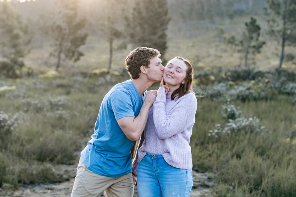 hombre en camiseta azul de cuello redondo besando a mujer en camisa blanca de manga larga durante el día