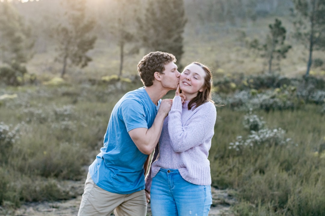 man in blue crew neck t-shirt kissing woman in white long sleeve shirt during daytime