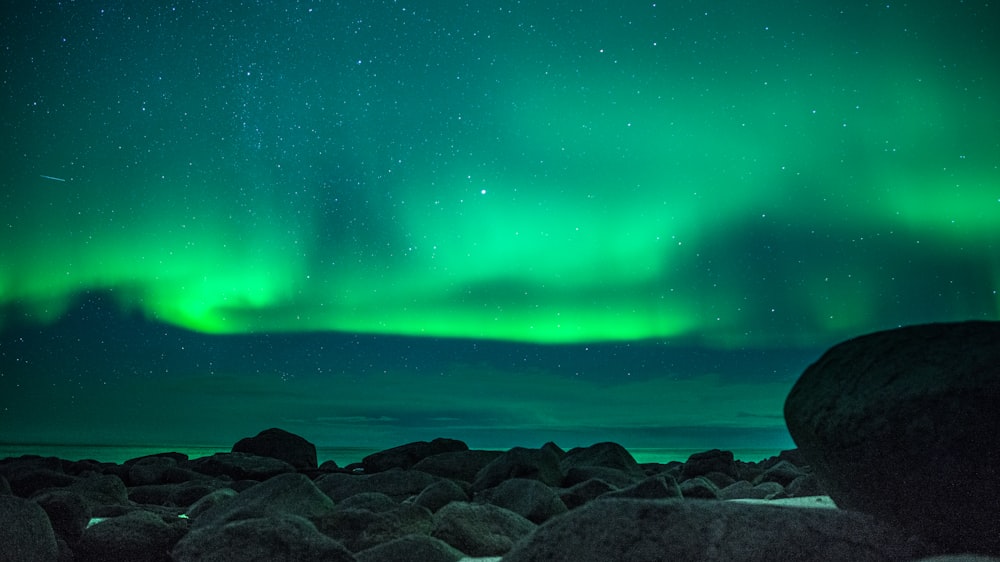 black rocks near body of water under green sky