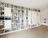 A spacious room with a large built-in bookshelf covering the entire wall, filled with various books, records, and decorative items. The shelves are predominantly white, creating a clean and modern look. The floor is wooden, and a couple of framed pictures are hung on the adjacent wall. Some shelves hold electronic devices and some have closed doors.