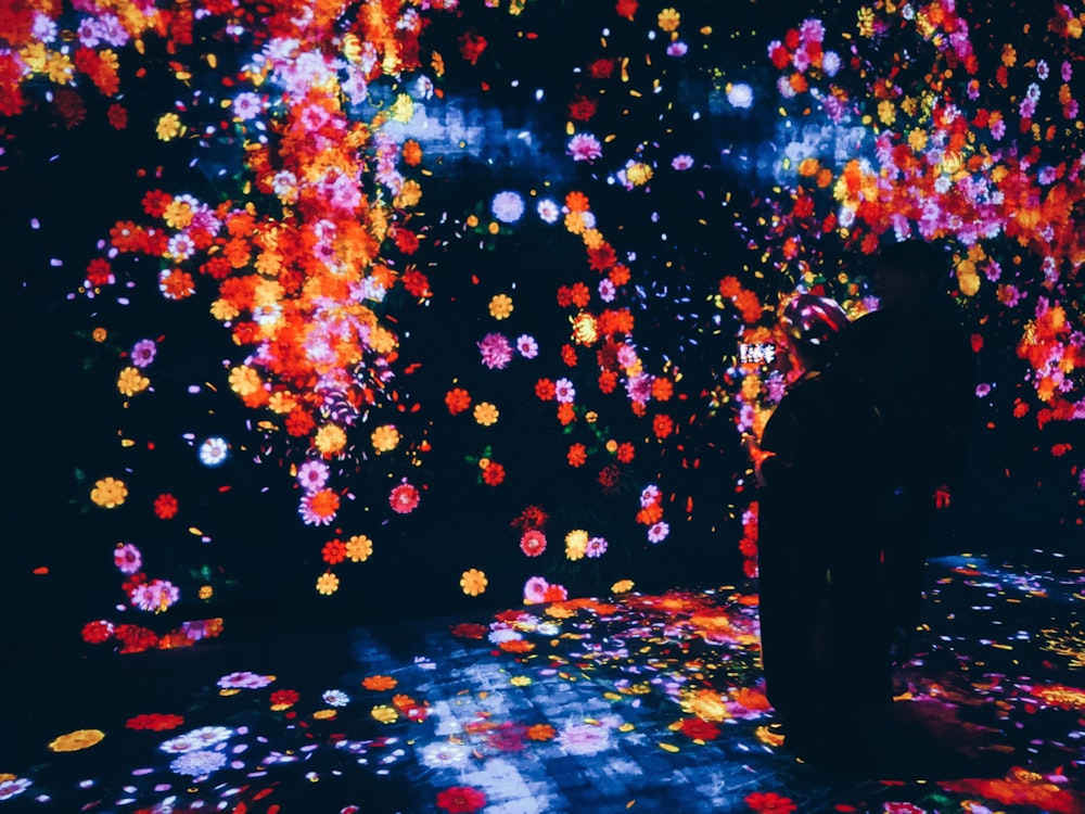 man in black jacket standing on the street with yellow and red lights