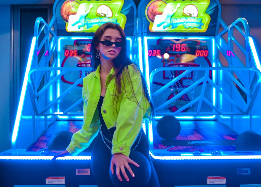 woman in yellow jacket and black pants sitting on blue and purple arcade machine