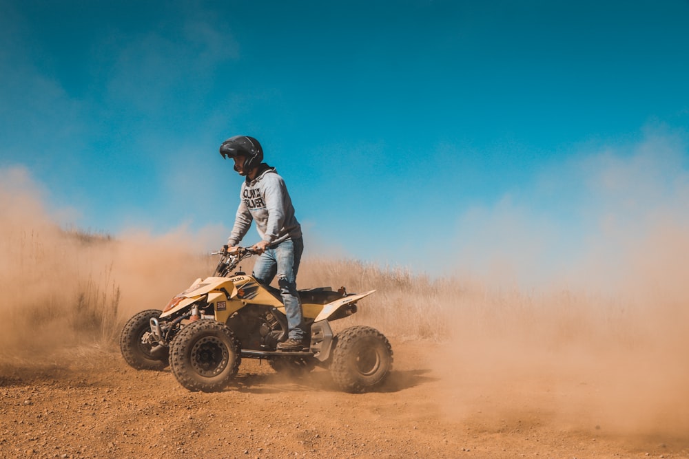 Mann fährt tagsüber auf gelbem ATV auf braunem Rasen