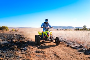 man riding blue and yellow atv on brown field under blue sky during daytime