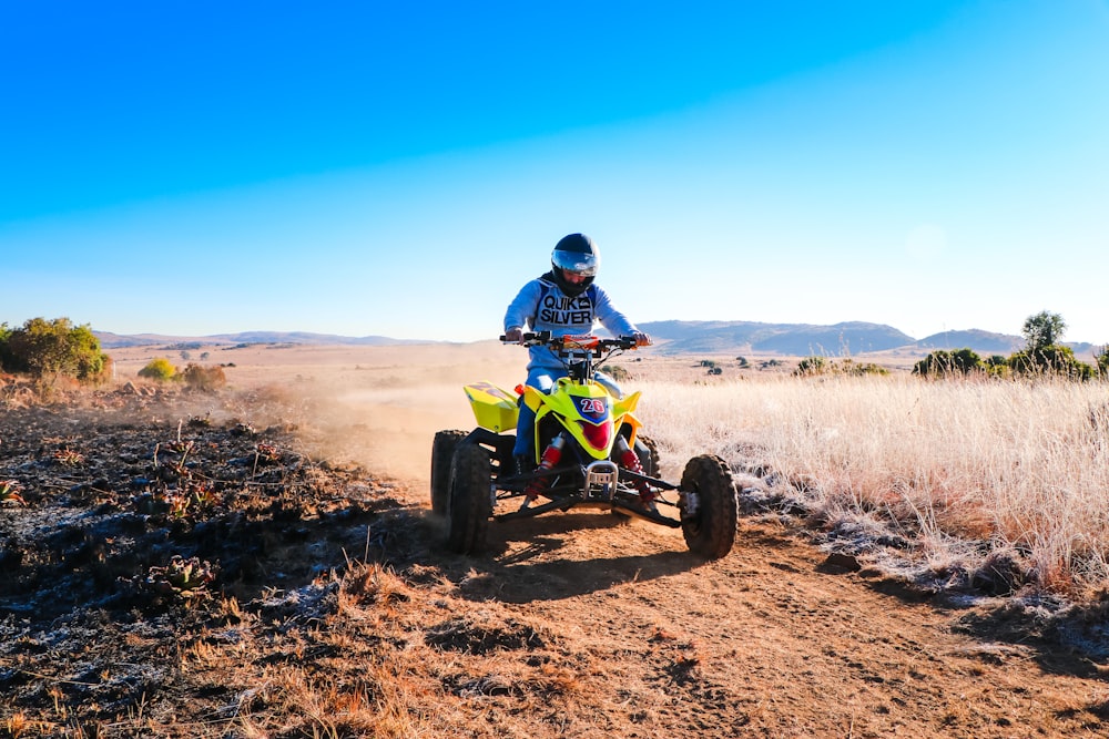 Uomo che guida ATV blu e giallo sul campo marrone sotto il cielo blu durante il giorno