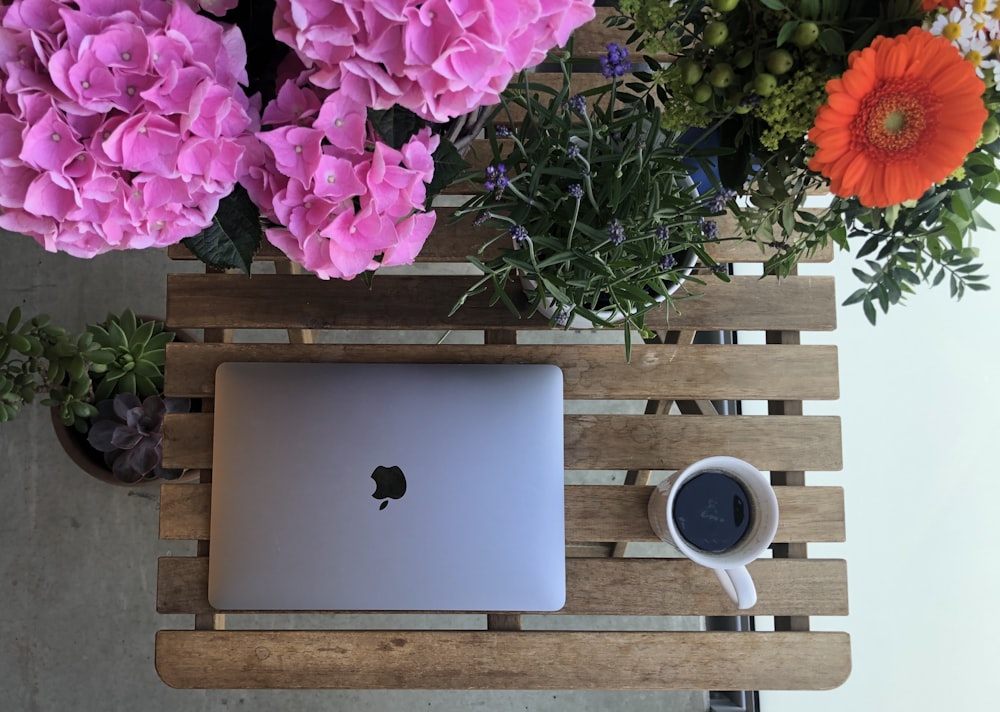 silver macbook beside white ceramic mug on brown wooden table