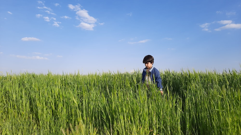 boy in blue jacket standing on green grass field under blue sky during daytime