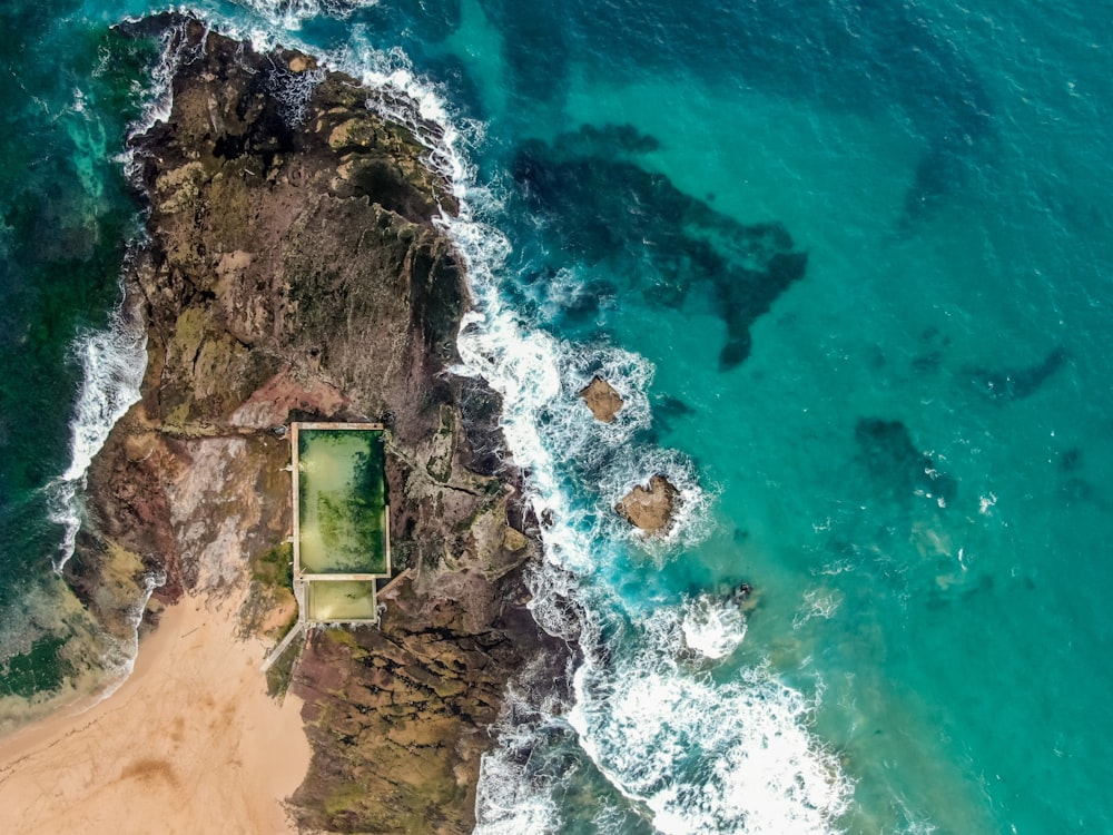 水域の近くの茶色の岩だらけの海岸にある緑と茶色の家の航空写真