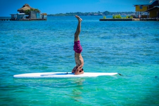 woman in purple shorts and black tank top doing yoga on white surfboard during daytime