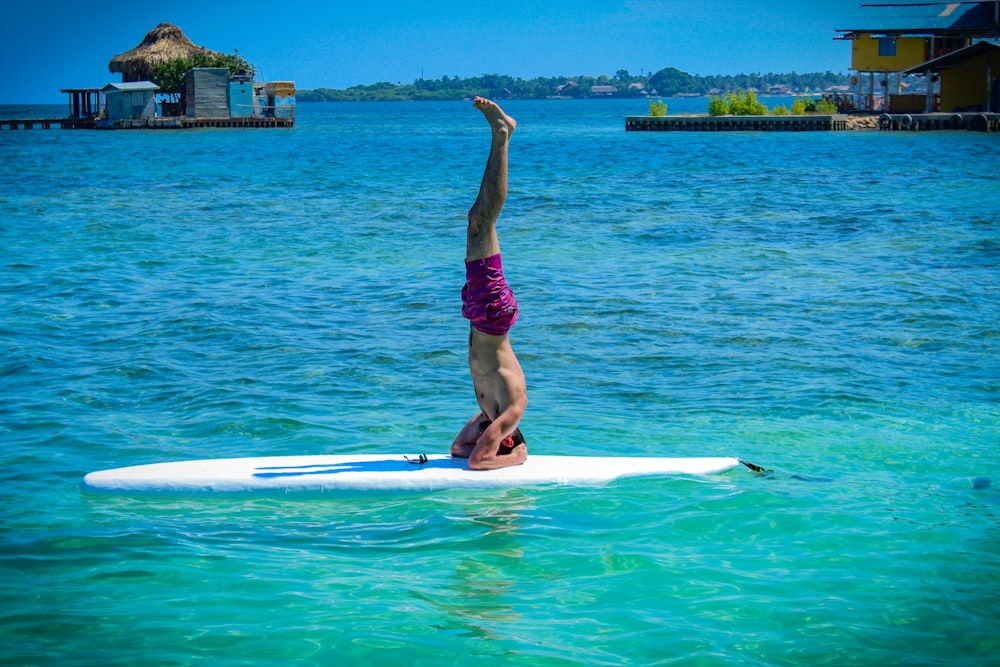 woman in purple shorts and black tank top doing yoga on white surfboard during daytime