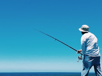 man in white shirt and blue denim jeans holding black fishing rod