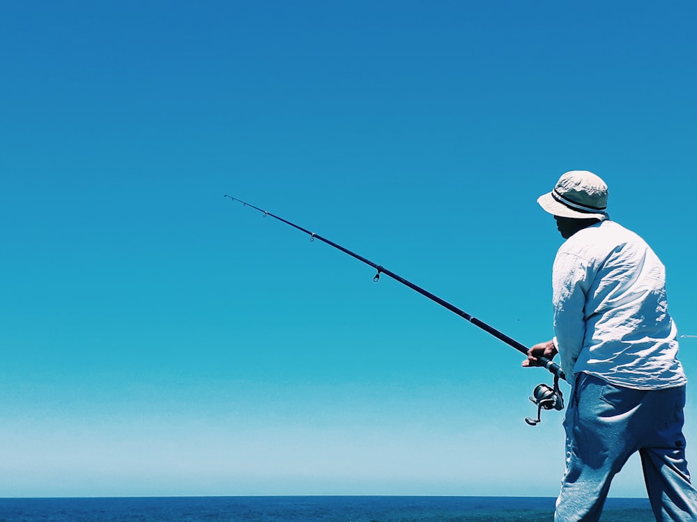 man in white shirt and blue denim jeans holding black fishing rod