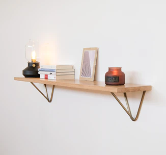 A sleek walnut wood wall shelf mounted in a bright modern living room with beige and white tones.