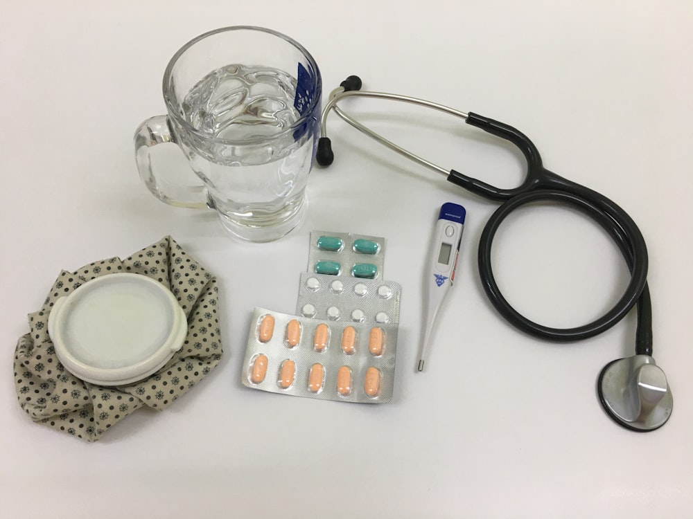 black and silver stethoscope beside clear glass mug