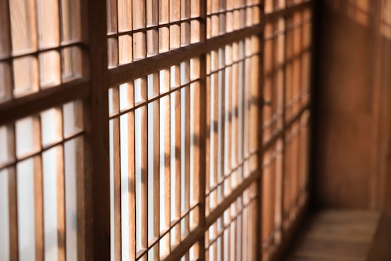 Wooden lattice panels create a grid-like pattern, with warm natural light casting shadows through the slats. The structure suggests a traditional architectural style, perhaps part of a sliding door or window.