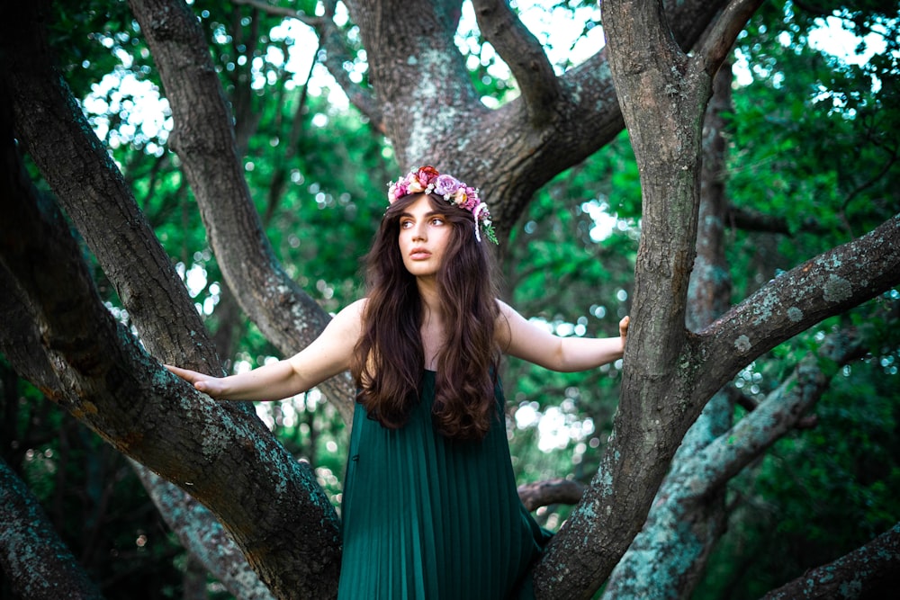 woman in green sleeveless dress wearing red floral headdress standing beside brown tree